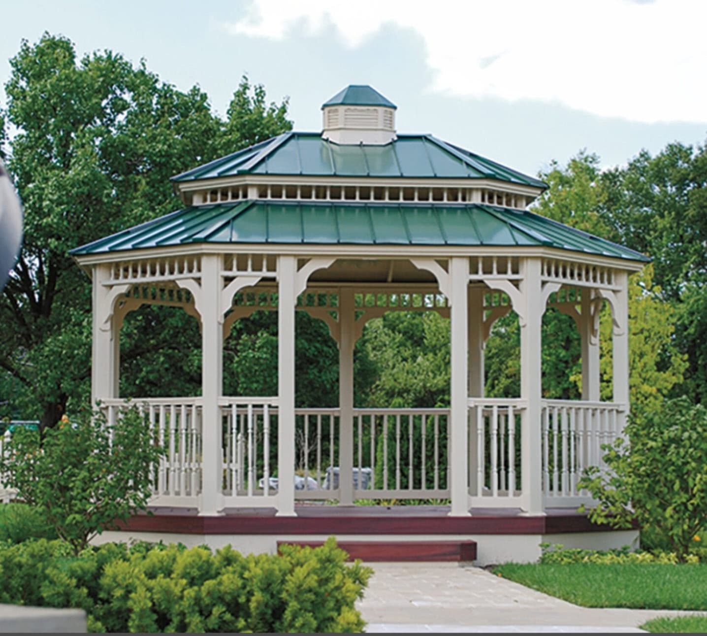White gazebo with a green metal roof in a landscaped garden