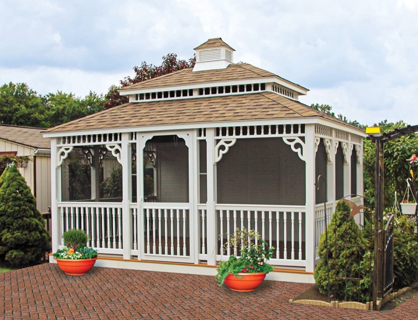 White screened gazebo with a shingle roof on a brick patio